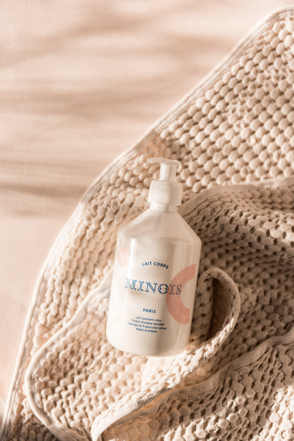 A Minois pump bottle lying on a cream knitted blanket in soft daylight | Botā natural skincare.