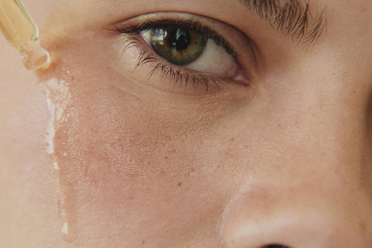 Close-up of an eye with a drop of clear serum running down the cheek