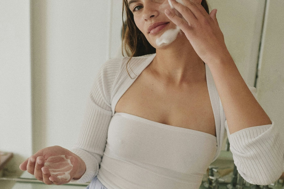 Applying skincare at a bathroom mirror in morning light
