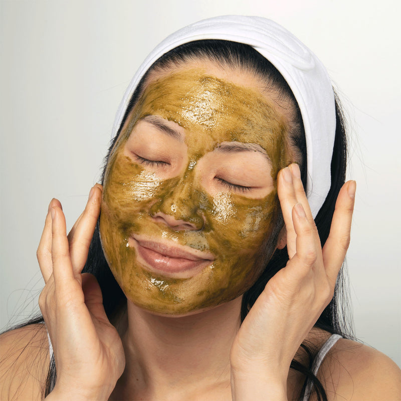 Woman with eyes closed wearing a green matcha face mask and a white headband