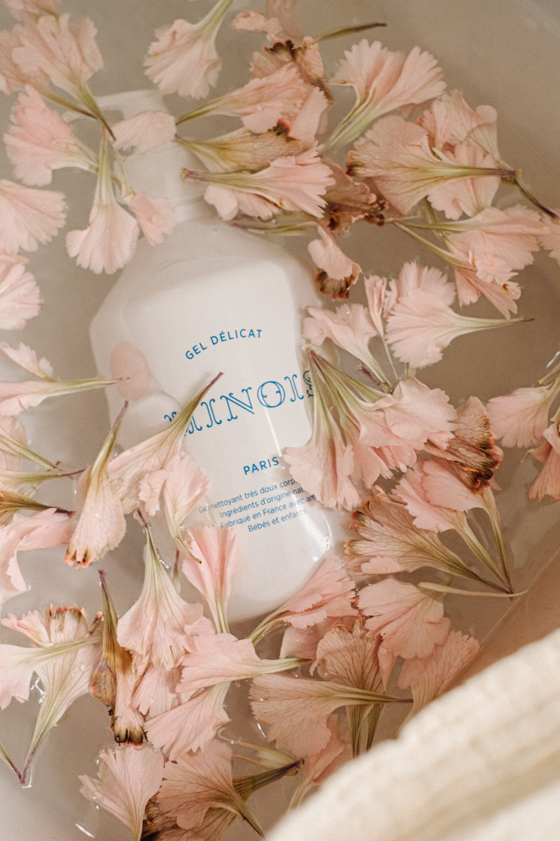 Minois Gel Délicat bottle lying among pale pink flowers