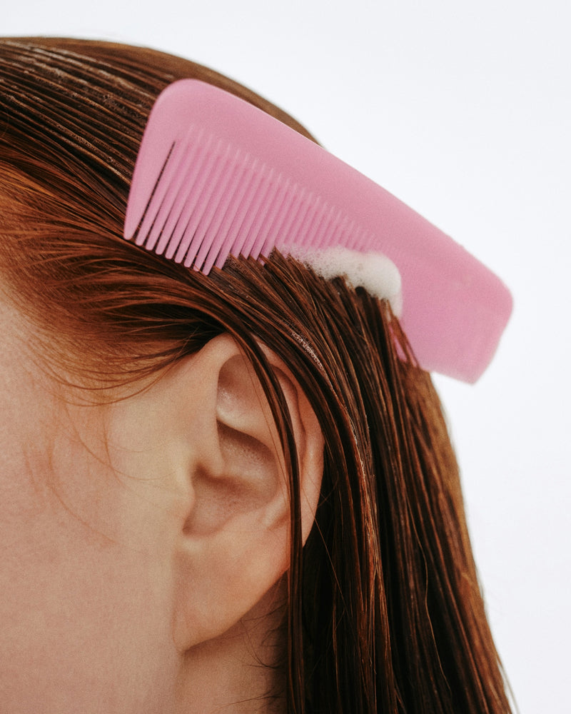 Pink comb drawn through wet auburn hair