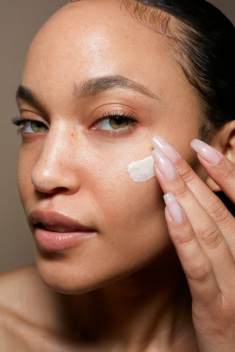 Le Prunier cream smoothed onto a cheek in close-up, fingertips resting on the skin | Botā natural skincare.