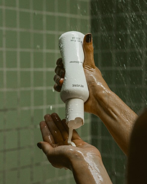 Hands dispensing Reverie Lightweight Nourishing Conditioner into a palm in the shower